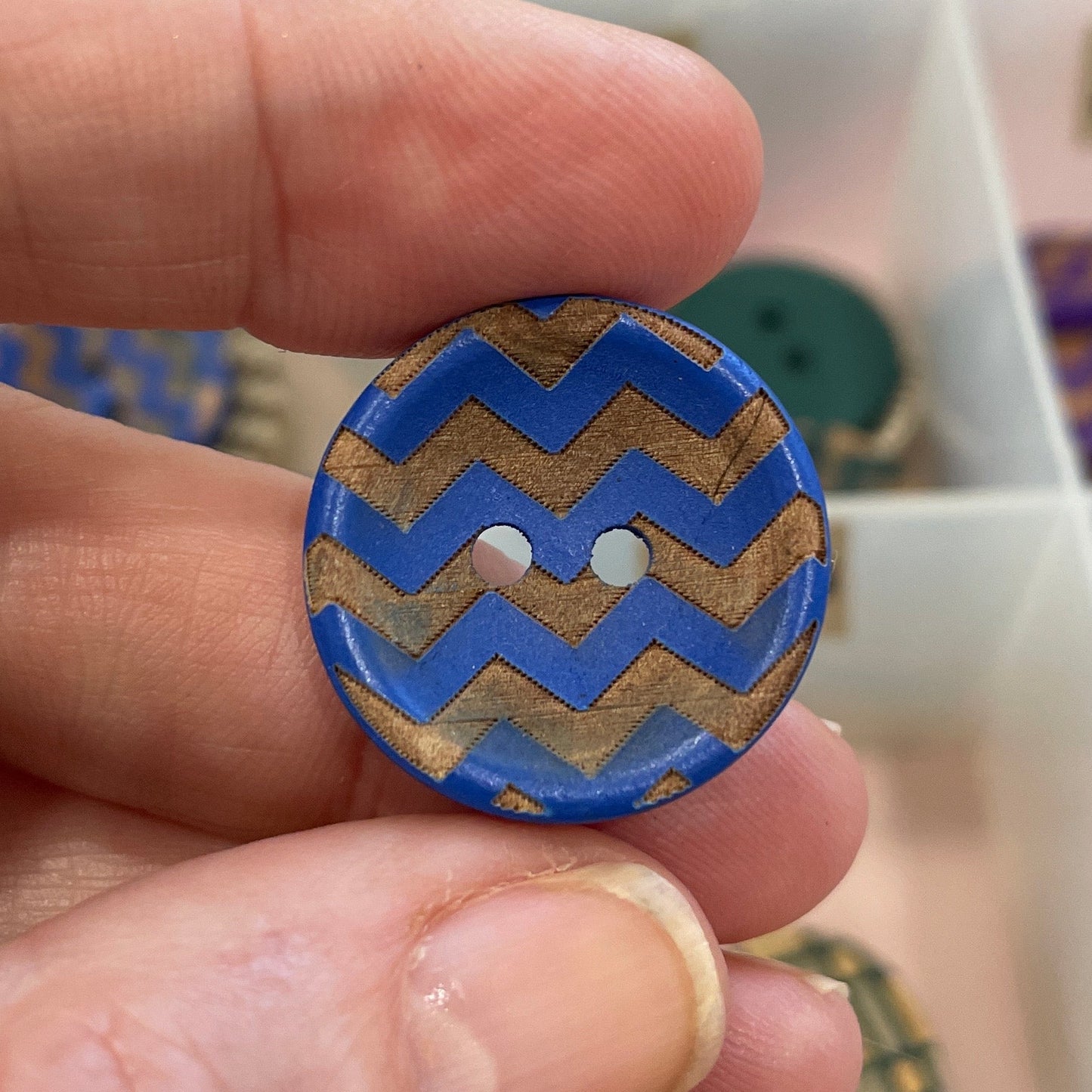 Hand holding a blue and gold zigzag patterned button with a blurred background of similar buttons.
