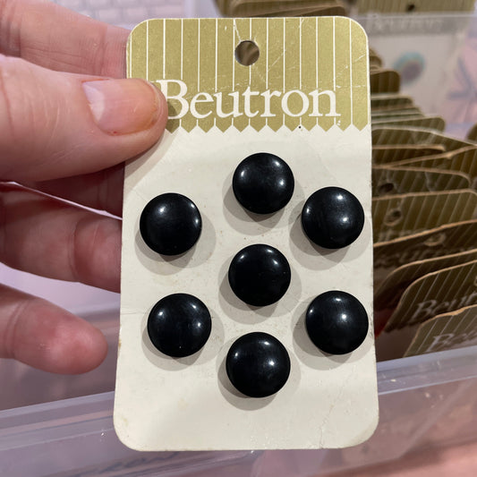 Card with six black buttons held by a hand against a blurred background