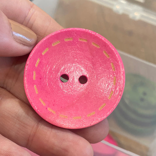Pink button held by a hand with a container of pink buttons in the background.