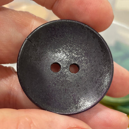Hand holding a black button with blurred background of buttons and fabric