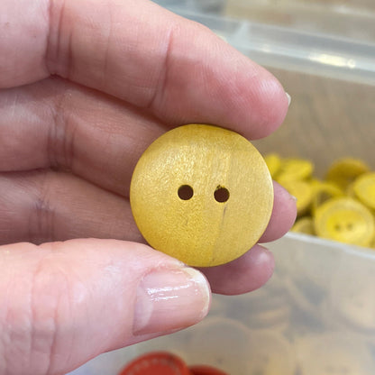 Hand holding a yellow button with a container of red buttons in the background