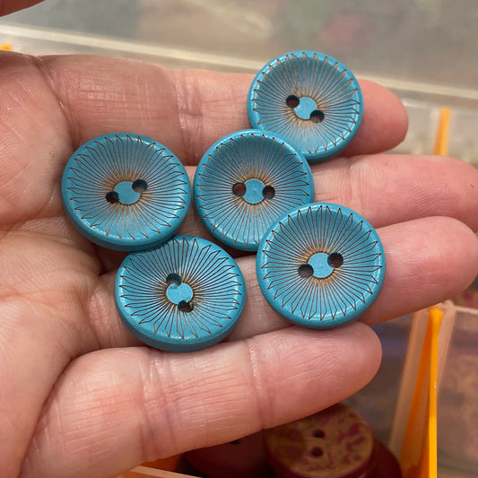 Hand holding blue buttons with a container of buttons in the background