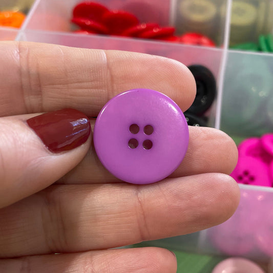 Hand holding a purple button with a clear container of buttons in the background