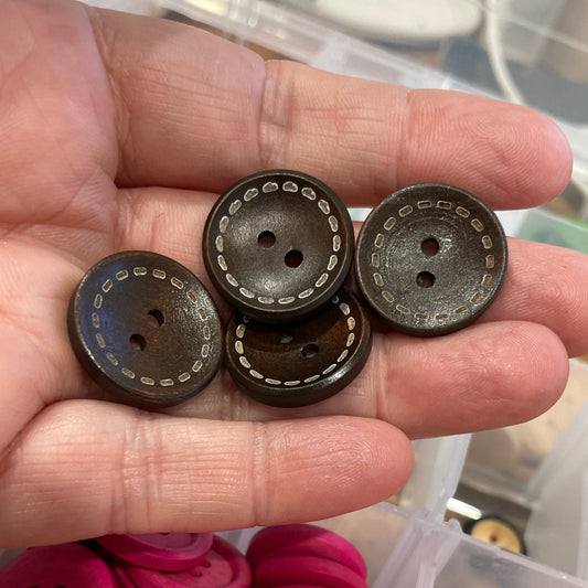 Hand holding buttons with a container of assorted buttons in the background