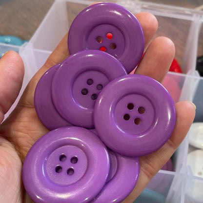 Hand holding four purple buttons with a blurred background of buttons and containers.