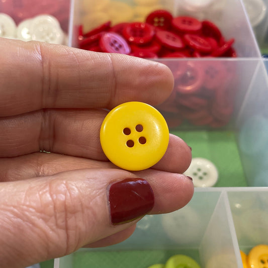 Hand holding a yellow button with a container of colorful buttons in the background