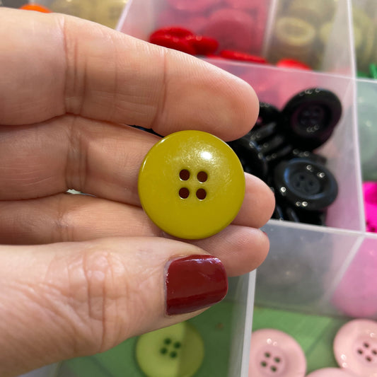 Hand holding a yellow button with a clear container of assorted buttons in the background