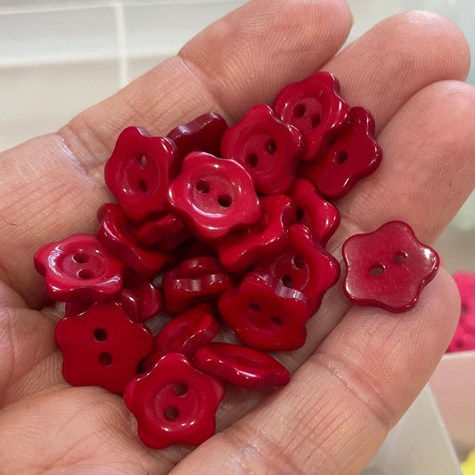 Hand holding red floral buttons with a container of similar buttons in the background.